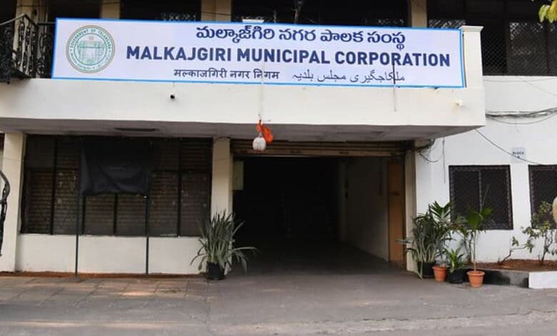 Entrance of Malkajgiri Municipal Corporation building with signage in multiple languages.