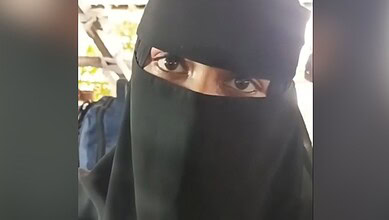 Muslim woman wearing a black niqab with only her eyes visible at a public event.