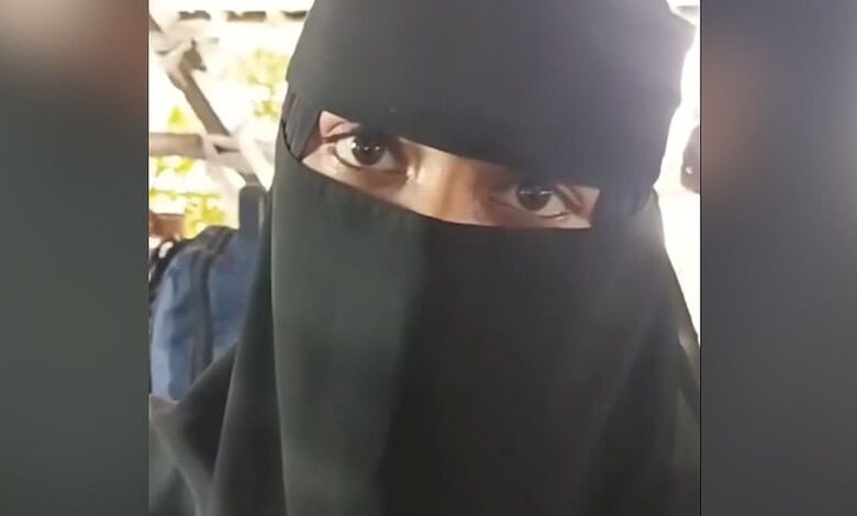 Muslim woman wearing a black niqab with only her eyes visible at a public event.