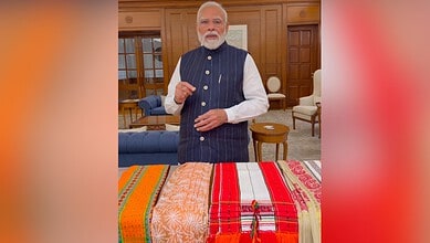 Prime Minister Narendra Modi in a formal setting with traditional handloom fabrics displayed.
