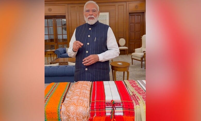 Prime Minister Narendra Modi in a formal setting with traditional handloom fabrics displayed.