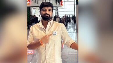 Naveen Pettem at an airport, wearing a white shirt and pointing to a badge.