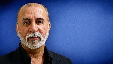 Close-up portrait of a middle-aged man with a beard and short hair against a blue background.