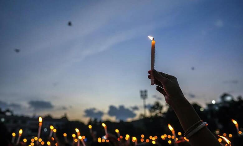 Person holding a lit candle during a memorial vigil at dusk in West Bengal.