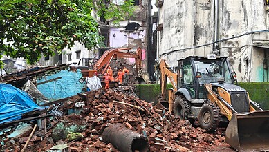 Construction workers demolish a building in Bhiwandi amid debris and machinery.