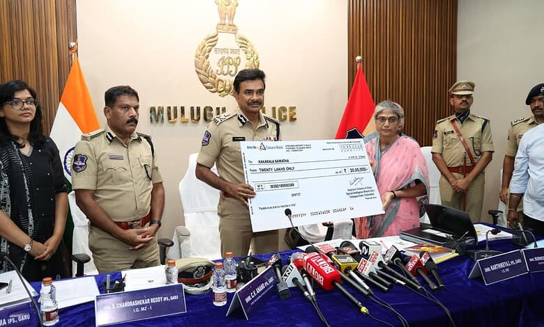 Telangana DGP Anand with officials and Maoists during Mulugu interaction, holding a cheque.