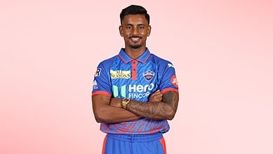 Delhi Capitals cricket player Abhishek Porel in team jersey smiling with arms crossed.
