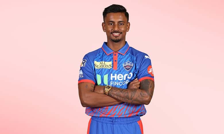 Delhi Capitals cricket player Abhishek Porel in team jersey smiling with arms crossed.