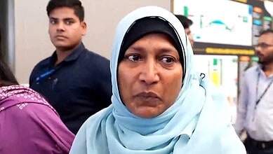 Woman in a light blue hijab at an indoor event with people in the background.