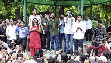 Group of people gathered outdoors at a public event, some taking photos and videos.