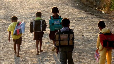 Children walking on a dusty road with backpacks, heading to school.