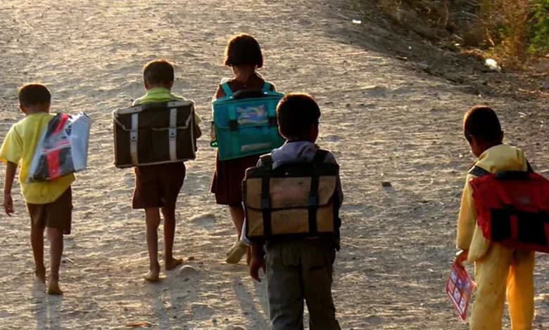 Children walking on a dusty road with backpacks, heading to school.
