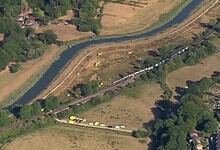 Aerial view of a derailed train near a river in England, with emergency responders present.