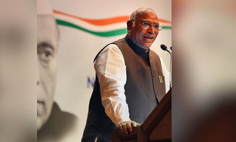 Kharge speaking at a podium during a political event, with a large banner in the background.
