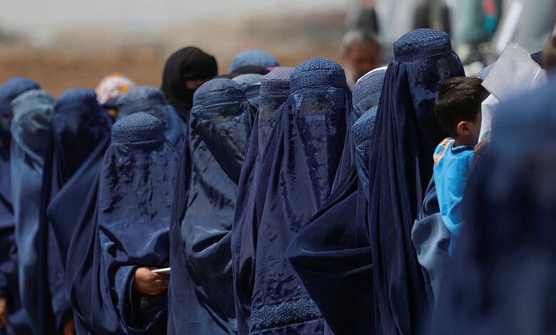 Afghan girls in blue burqas gather outdoors, some with children, under a clear sky.