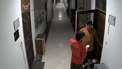 Two men in a corridor, one knocking on a door, the other holding a paper, in a residential building.