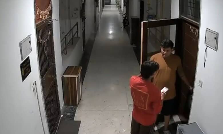 Two men in a corridor, one knocking on a door, the other holding a paper, in a residential building.