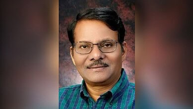 Portrait of a man with glasses, wearing a blue checkered shirt, smiling at the camera.