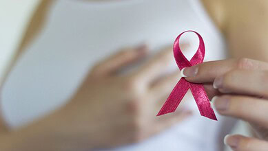 Person holding pink ribbon symbol for breast cancer awareness close to chest.