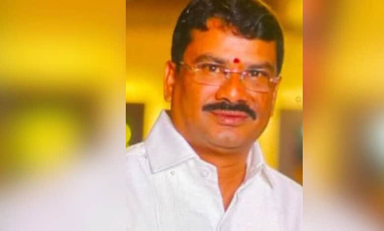 Man in white shirt with glasses and red tilak, smiling at camera.