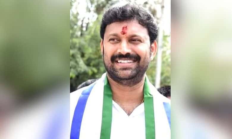 Smiling man with a red tilak on forehead, wearing a white shirt and green scarf.