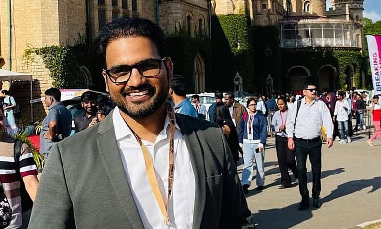 Smiling man in sunglasses and suit at outdoor event with historic building background.