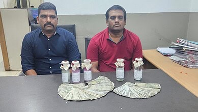 Two men seated at a table with confiscated drugs and cash displayed in front of them.