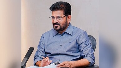 Revanth during a meeting, wearing a blue shirt and glasses, in an office setting.