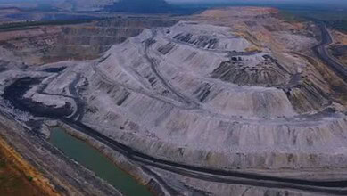 Large open-pit coal mine with terraced excavation and water bodies in Telangana, India.
