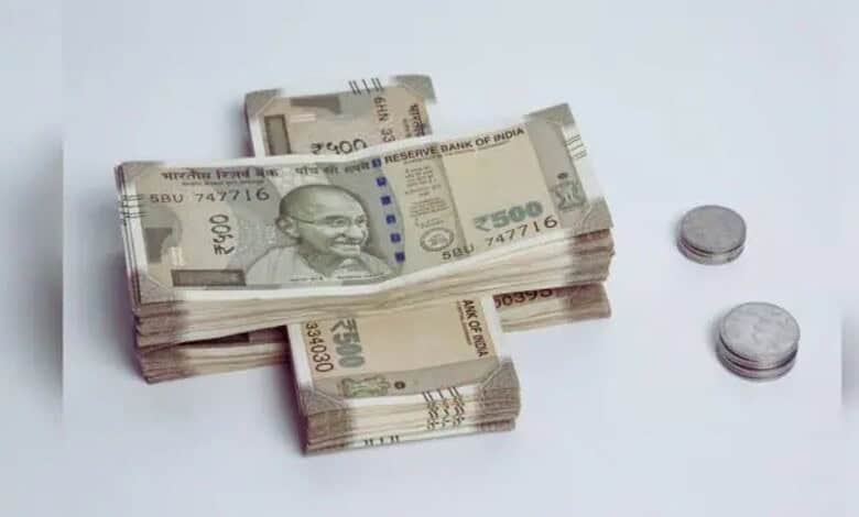 Stacks of Indian 500 rupee notes and coins on a white surface.