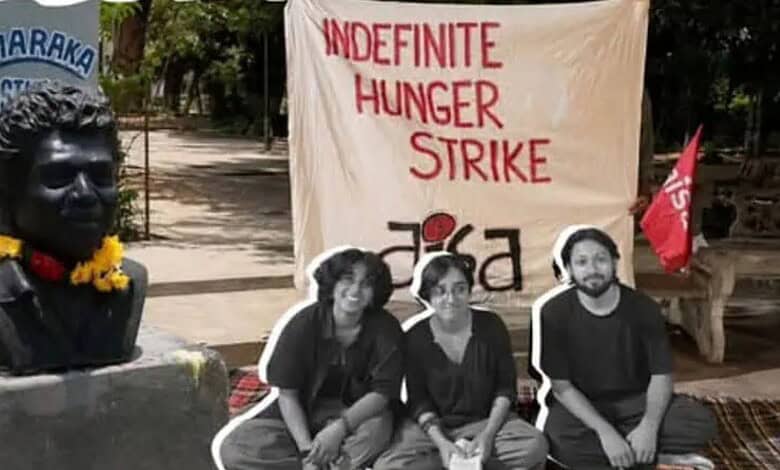 Protesters with a banner for indefinite hunger strike and a bust statue in the background.
