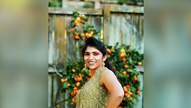 Smiling woman in traditional attire standing outdoors with orange trees in the background.
