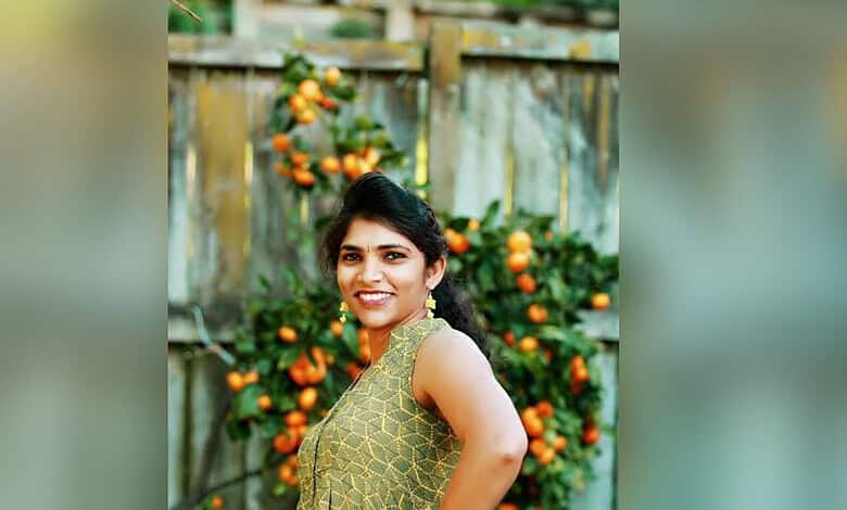 Smiling woman in traditional attire standing outdoors with orange trees in the background.