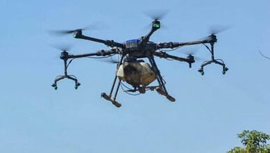 Unmanned drone flying in clear blue sky with visible propellers and sensors.