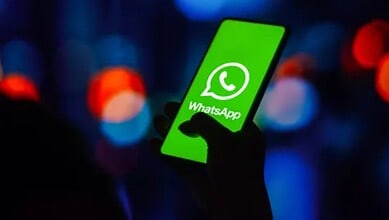 Person holding a smartphone displaying the WhatsApp logo with a dark, blurred background.