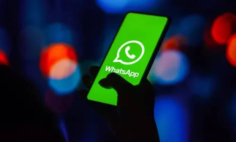 Person holding a smartphone displaying the WhatsApp logo with a dark, blurred background.
