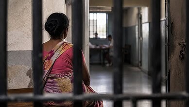 Woman in traditional saree sitting in a prison corridor with barred gates.