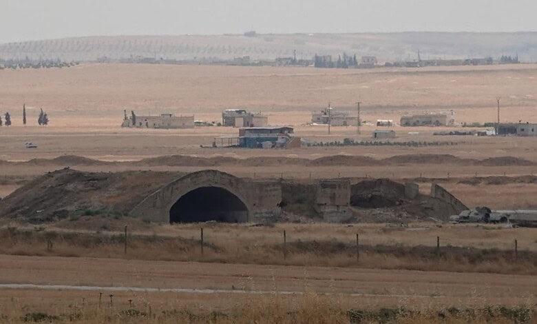 Underground military tunnel in arid desert with distant buildings and infrastructure.