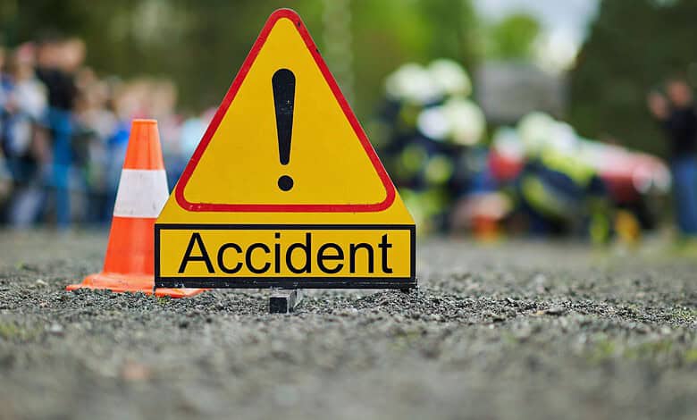 Accident scene with warning sign and blurred emergency responders in background.