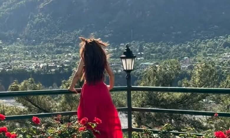 Woman in a red dress overlooking a scenic valley with mountains and greenery.