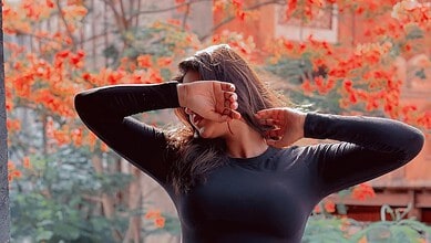 Woman with long hair in black top covering her face with her hand outdoors in autumn.