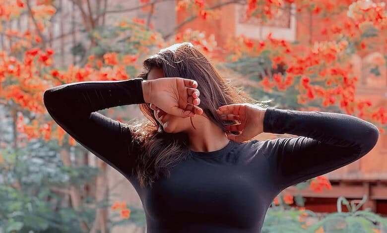 Woman with long hair in black top covering her face with her hand outdoors in autumn.