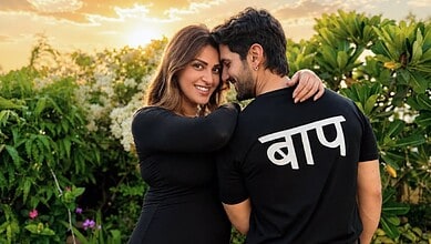 Happy couple embracing outdoors, woman smiling, man with 'Bapu' written in Hindi on his shirt.