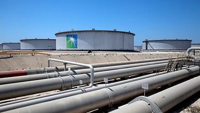 Large storage tanks at Saudi Aramco refinery under clear blue sky.