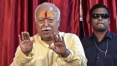 Bhagwat speaking to youth with hands raised, wearing yellow kurta and tilak on forehead.