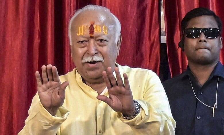 Bhagwat speaking to youth with hands raised, wearing yellow kurta and tilak on forehead.