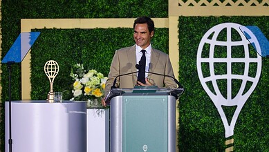 Roger Federer smiling at podium during Hall of Fame speech with awards and greenery behind him.