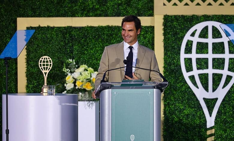Roger Federer smiling at podium during Hall of Fame speech with awards and greenery behind him.