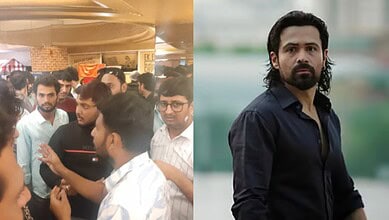 Crowd of people gathered indoors, some engaged in conversation, with a man in a white shirt speaking.