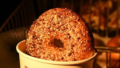 Close-up of a sprinkled bagel in a white cup on a dark background.